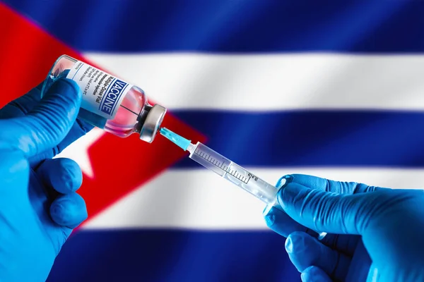 Doctor preparing vial of vaccine injection for the vaccination plan against diseases in Cuba. Injecting dose of vaccine in syringe for infections prevention in front of the Cuba flag