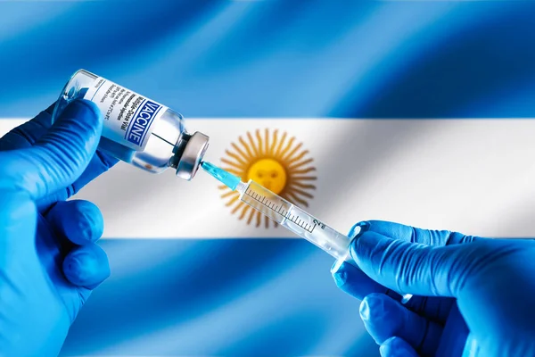 Doctor preparing vial of vaccine injection for the vaccination plan against diseases in Argentina. Injecting dose of vaccine in syringe for infections prevention in front of the Argentina flag