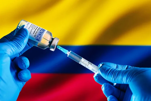 Doctor preparing vial of vaccine injection for the vaccination plan against diseases in Colombia. Injecting dose of vaccine in syringe for infections prevention in front of the Colombia flag