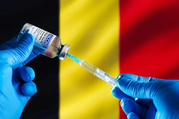 Doctor preparing vial of vaccine injection for the vaccination plan against diseases in Belgium. Injecting dose of vaccine in syringe for infections prevention in front of the Belgium flag