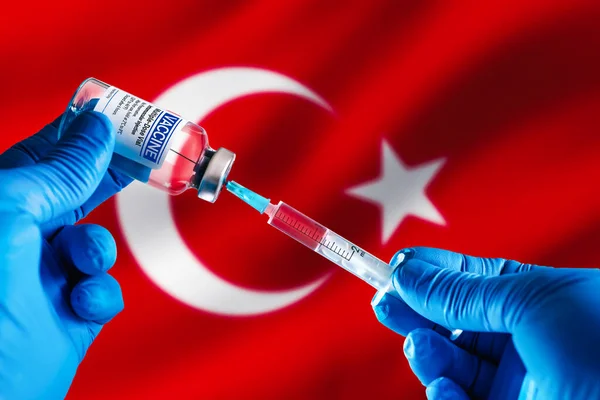 Doctor preparing vial of vaccine injection for the vaccination plan against diseases in Turkey. Injecting dose of vaccine in syringe for infections prevention in front of the Turkish flag