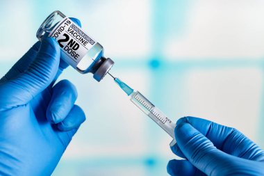 Coronavirus aşısı şişesi olan doktor etiketinde ikinci doz aşının adı yazılı. Doktor Covid-19 'un ikinci aşısı için bir doz hazırlıyor.