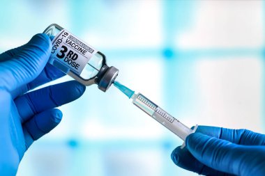 Coronavirus aşısı şişesi olan doktor. Etiketinde üçüncü doz aşının adı yazıyor. Doktor, Covid-19 aşısının üçüncü aşısı için bir doz hazırlıyor.