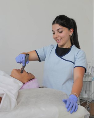 Olgun bir kadın modern güzellik kliniğinde ya da spa salonunda bir kozmetik uzmanı tarafından yapılan profesyonel bir yüz bakımı alıyor..
