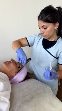 Olgun bir kadın modern güzellik kliniğinde ya da spa salonunda bir kozmetik uzmanı tarafından yapılan profesyonel bir yüz bakımı alıyor..