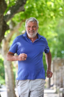 Neşeli yaşlı Latin adam arka planda yemyeşil bir havayla dışarıda koşuyor..