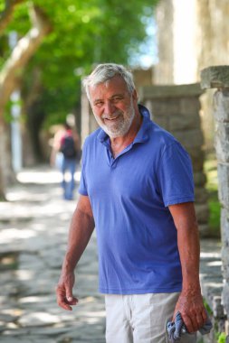 Arka planda yemyeşil bir yeşillikle dışarıda gülümseyen neşeli, son sınıf Latin bir adamın portresi..