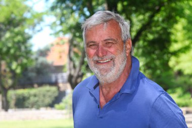 Arka planda yemyeşil bir yeşillikle dışarıda gülümseyen neşeli, son sınıf Latin bir adamın portresi..