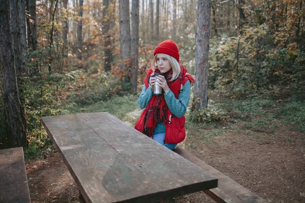 女背包客坐在有桌子的木制长椅上 在森林里喝咖啡 — 图库照片
