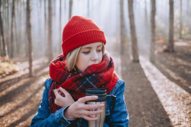 Ormanda kahve içen sırt çantalı bir kadın düşmüş bir kütüğün üzerinde oturuyor.