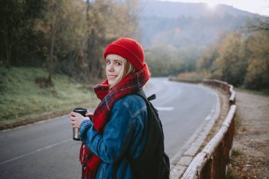 Sonbaharda bir dağ yolunda yürüyen ve kahve içen bir kadın.