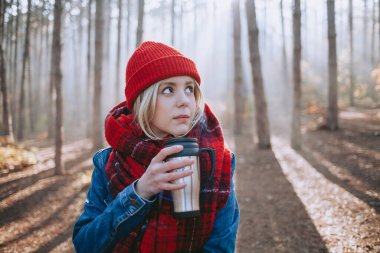 Ormanda kahve içen sırt çantalı bir kadın düşmüş bir kütüğün üzerinde oturuyor.