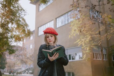 Okul kampüsünde kitap okuyan genç bir öğrenci. Sonbaharda Avrupa Üniversitesi 'nde kırmızı bereli bir kadın.