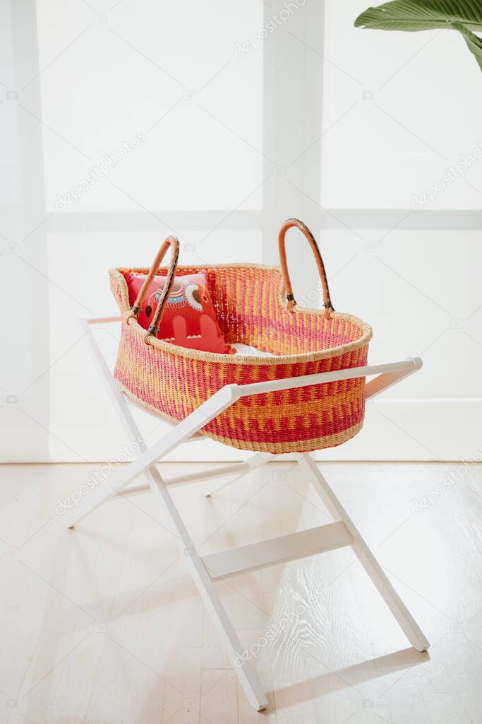 Baby basket in a bright kids' room. Nobody. Closeup of empty babygirl cradle.