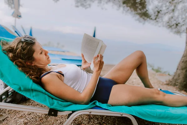 Woman sunbathing and reading at the beach at the ocean — Fotografia de Stock