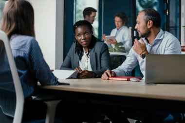 Parlak, cam duvarlı bir ofisteki bir toplantıda çeşitli profesyoneller. Farklı ırkların, cinsiyetlerin ve yaşların takım üyeleri bir konferans masası etrafında tartışılır.. 