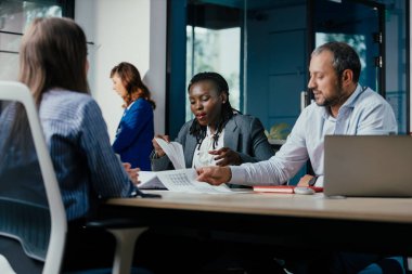 Professional multiracial team engaged in dynamic project discussion in contemporary urban office space with glass windows, showcasing inclusive workplace culture and modern corporate environment.