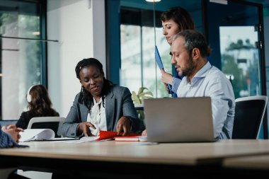 Çeşitli iş adamları ofis toplantısında strateji ve evrak işlerini tartışıyor.