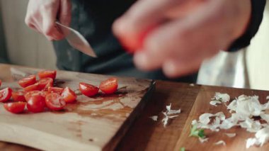 Bir aşçının eli ahşap bir kesme tahtasının üzerinde domatesleri yavaş çekimde doğruyor.