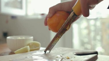 Kadın ellerinin portakal kabuğunu ızgarayla ızgara yaptığı yakın plan. Mutfaktaki tahta kesme tahtasının üzerinde zester var.