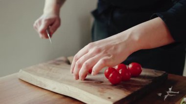 Şefin ellerini yavaşça tahta bir tahtada taze vişne domateslerini keserken yaklaş.