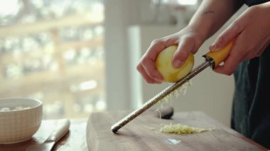 Parlak bir mutfakta limon kabuğunu rendeleyen kadın elleri yemek tarifi için zester bir aletle...