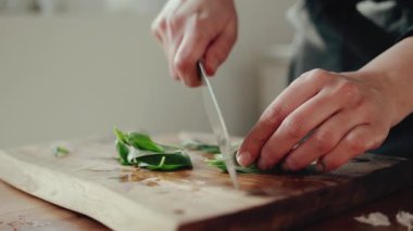 Yavaş çekimde ahşap bir kesme tahtasının üzerinde taze yeşil fesleğen doğrayan bir aşçının ellerine yaklaş.