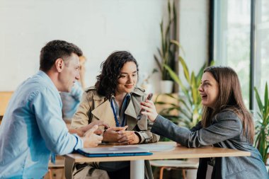 Üç farklı iş arkadaşı gülümsüyor ve akıllı bir telefona bakarken sohbet ediyorlar.