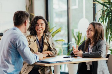 İş arkadaşları gayri resmi bir iş toplantısı sırasında masada konuşuyor ve gülümsüyor.
