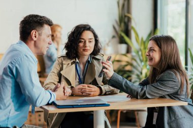 İş arkadaşları kahve molası sırasında akıllı telefon kullanarak tartışıyorlar.