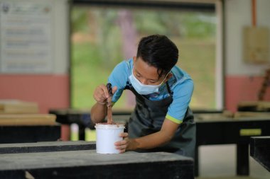 İş kıyafetleri ve yüz maskesi takan genç marangoz konsol masasında ahşap dolgu malzemesi kullanıyor. .