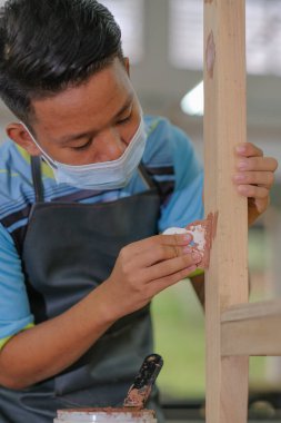 İş kıyafetleri ve yüz maskesi takan genç marangoz konsol masasında ahşap dolgu malzemesi kullanıyor. .