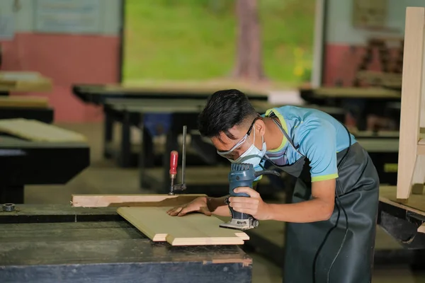 İş kıyafetleri ve yüz maskesi takan genç marangoz konsol masası yapmak için budayıcı kullanıyor. Seçici odak