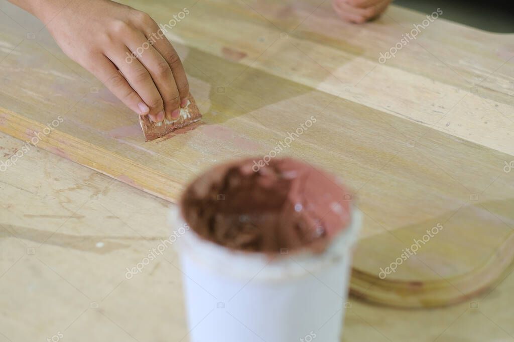 Young carpenter in work clothes and face mask  using wood filler in finishing work  for console table .