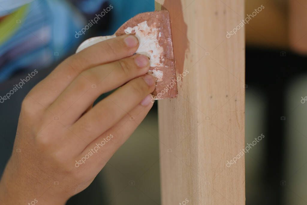 Young carpenter in work clothes and face mask  using wood filler in finishing work  for console table .