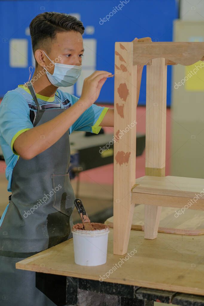 Young carpenter in work clothes and face mask  using wood filler in finishing work  for console table .