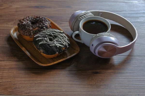 带耳机的美味甜甜圈和木制桌子上的咖啡 — 图库照片
