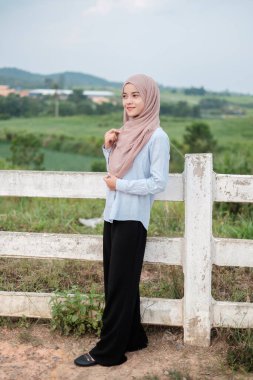 Yeşil çiftlik geçmişi olan mutlu ve güzel Asyalı bir kadının portresi. Duruyor ve gülümsüyor..