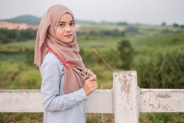 Steteskopla tesettürlü güzel bayan veteriner çiftlik ineğinin beyaz çitinin yanında duruyor.