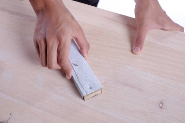 Genç marangoz beyaz arka planda izole edilmiş kanepe sunucusu projesinde zımpara kağıdı kullanıyor.