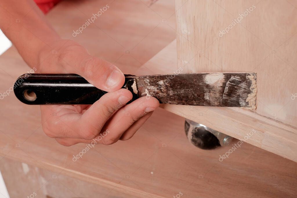 Young carpenter in work clothes  using wood filler in finishing work  for sofa server project isolated on white background