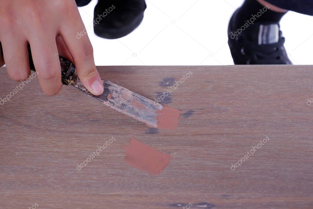 Young carpenter in work clothes  using scraper and wood filler in finishing work  for sofa server project isolated on white background