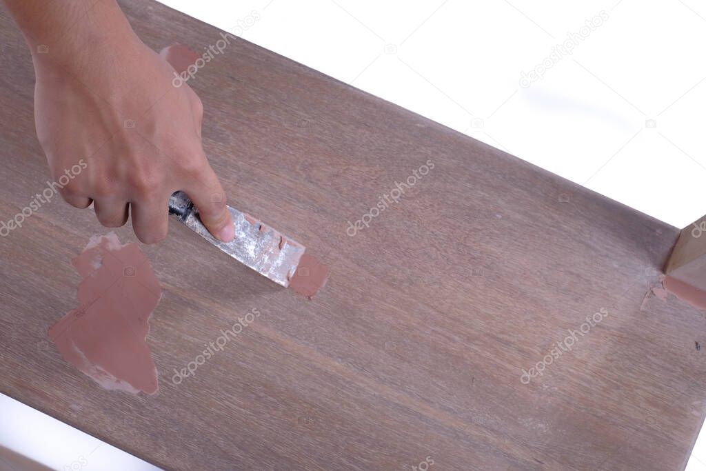 Young carpenter in work clothes  using scraper and wood filler in finishing work  for sofa server project isolated on white background