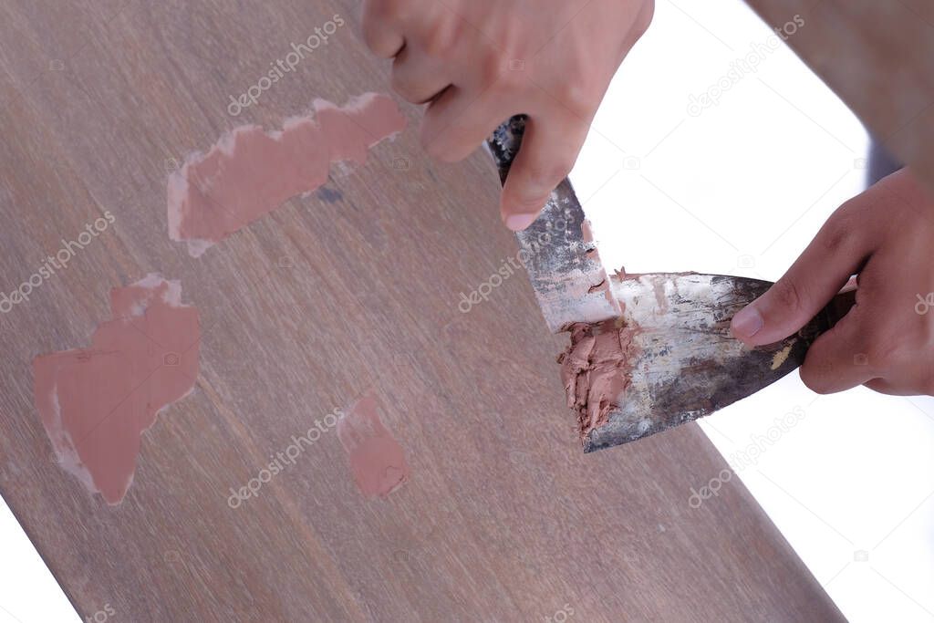 Young carpenter in work clothes  using scraper and wood filler in finishing work  for sofa server project isolated on white background