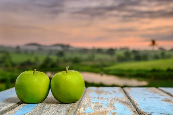 Two apples on wooden table in the sunlight with  a blurred nature  background.