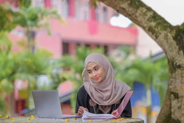 公園に座って銀製のラップトップを使用してスカーフを身に着けている美しいイスラム女性の学生の写真 — ストック写真