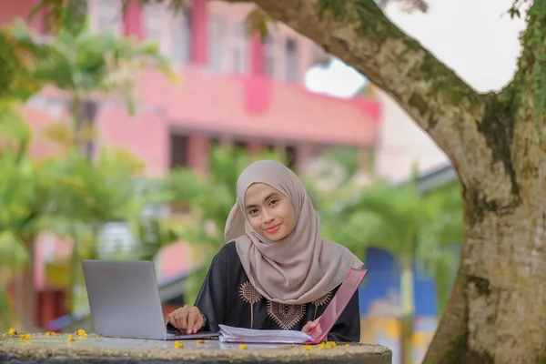 公園に座って銀製のラップトップを使用してスカーフを身に着けている美しいイスラム女性の学生の写真 — ストック写真