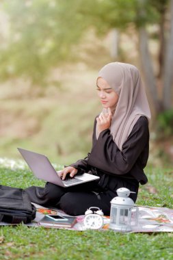 Yeşil parkta oturan ve gümüş dizüstü bilgisayar kullanan 20 'li yaşlarda güzel bir İslami öğrenci fotoğrafı..