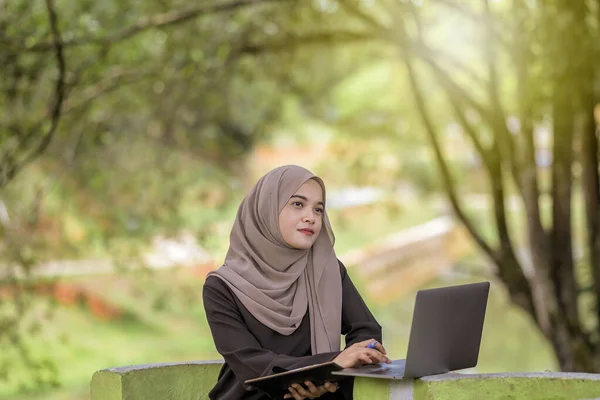 美しいイスラム女性の学生の写真20代は緑の公園に座っていると銀のラップトップを使用してスカーフを着て — ストック写真