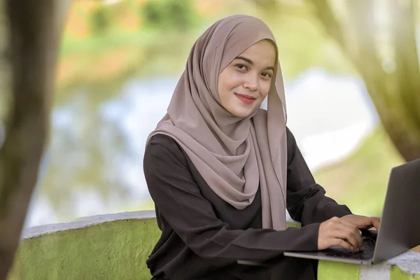 照片上美丽的伊斯兰女生20多岁 头戴头巾 坐在绿地公园里 用银色笔记本电脑 — 图库照片